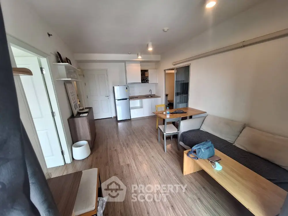 Modern open-layout living room with kitchen, featuring sleek furniture and wooden flooring.