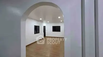 Spacious empty room with wooden flooring and arched entryway, ideal for customization.