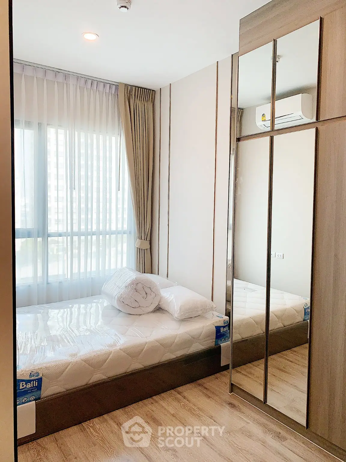 Modern bedroom with mirrored wardrobe and large window in a stylish apartment.