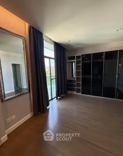 Spacious bedroom with large window and built-in wardrobe, featuring elegant hardwood flooring and modern design.