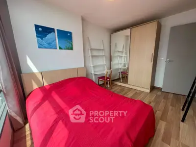 Cozy bedroom with red bedding, wooden flooring, and modern wardrobe in a bright apartment.