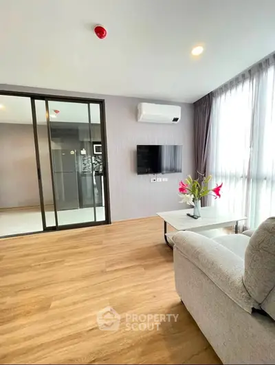 Modern living room with sleek design, featuring a wall-mounted TV, air conditioning, and large windows for natural light.