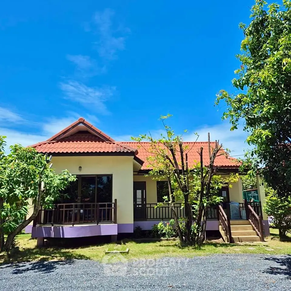 Charming single-story home with red-tiled roof and lush garden under clear blue sky.