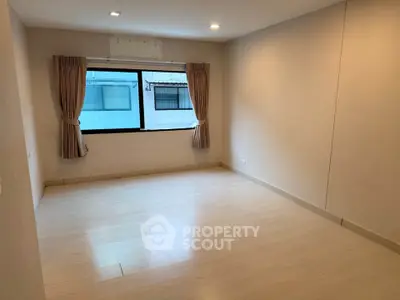 Spacious empty room with large window and wooden flooring, ideal for customization.