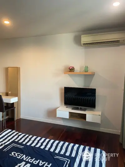 Modern bedroom with TV and air conditioning, featuring sleek wooden flooring and stylish decor.