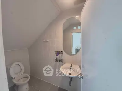 Modern bathroom with sleek design featuring a wall-mounted sink and oval mirror under sloped ceiling.