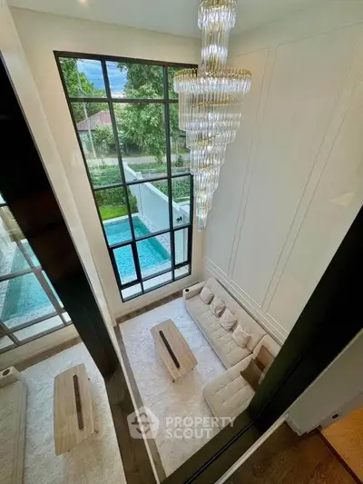 Luxurious living room with high ceiling, elegant chandelier, and pool view through large windows.