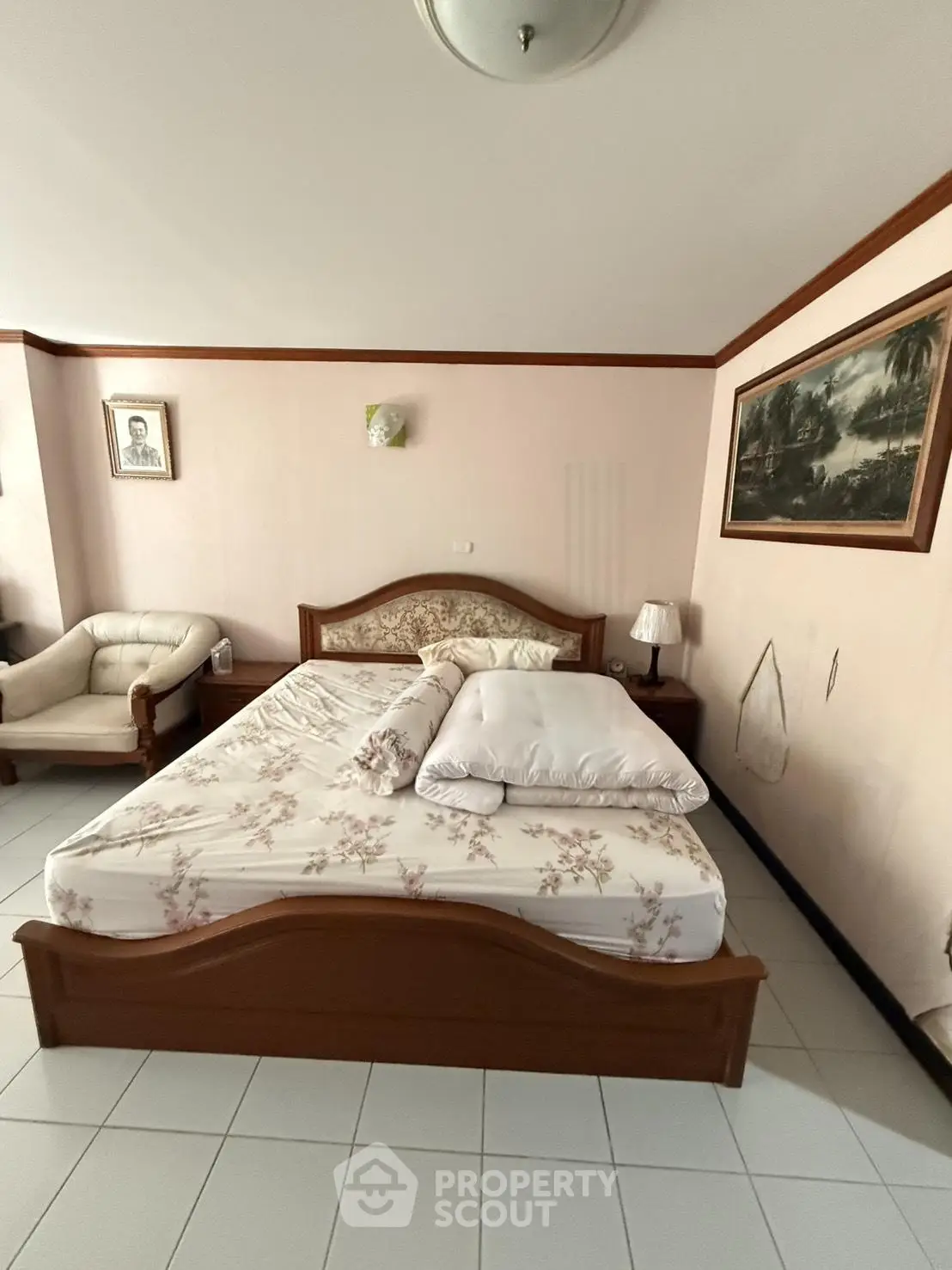 Cozy bedroom with elegant wooden bed frame and floral bedding, complemented by classic wall art and a comfortable armchair.