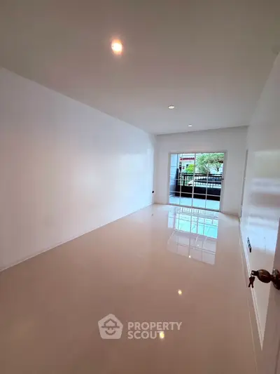 Spacious empty room with glossy floors and large sliding glass doors leading to balcony.