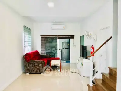 Modern living room with stylish sofa, TV, and sleek staircase in a bright, airy space.