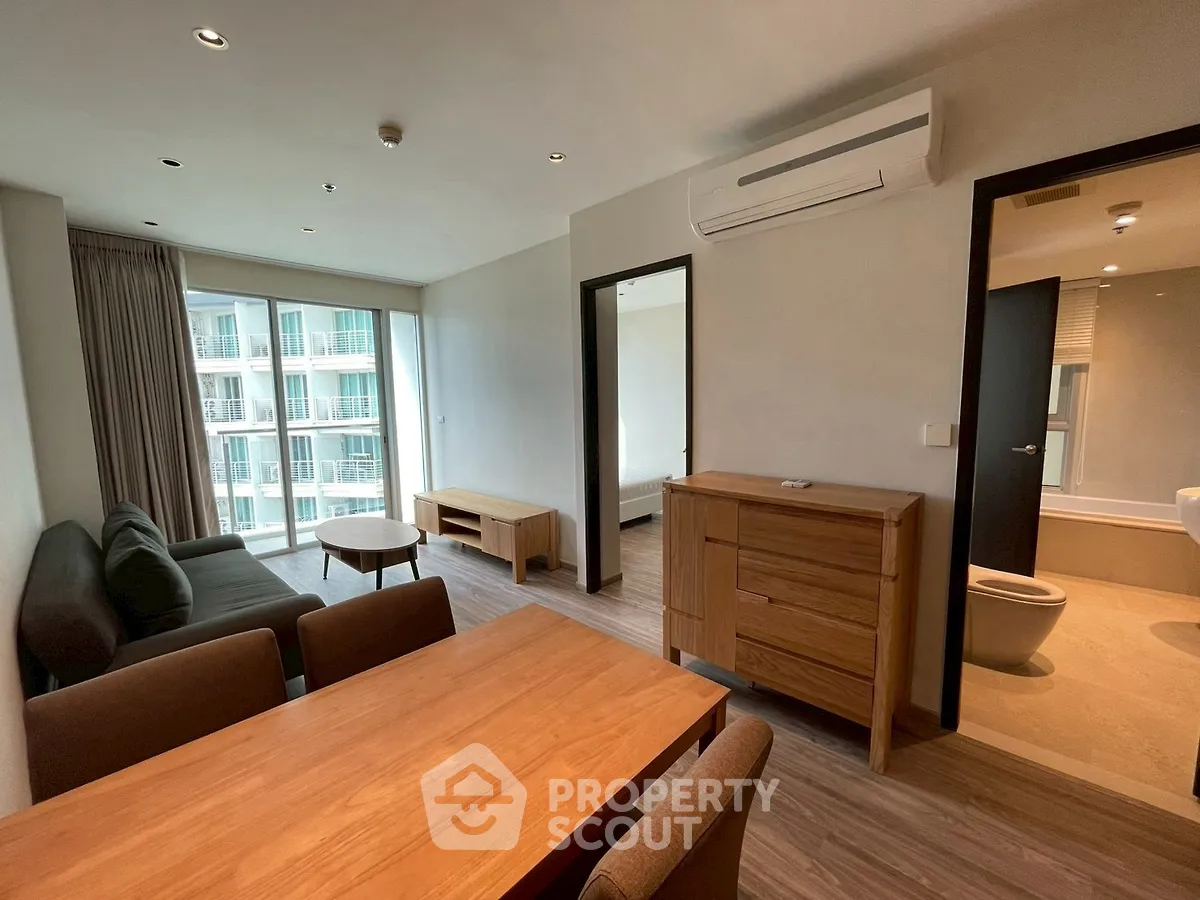 Modern apartment interior with open living and dining area, featuring wooden furniture and large windows.