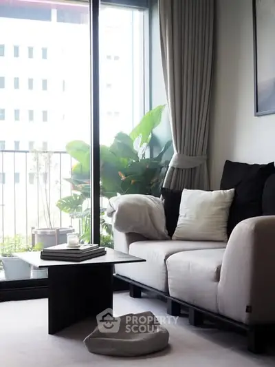 Modern living room with large windows and cozy seating area overlooking a balcony with lush greenery.