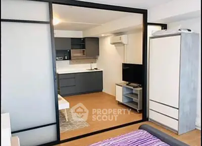 Modern studio apartment with sleek kitchen and cozy living area, featuring sliding glass doors and contemporary design.