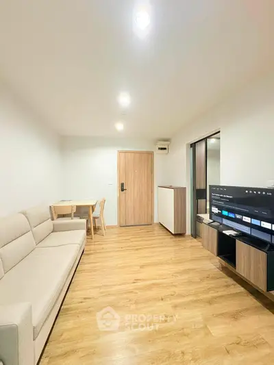 Modern living room with wooden flooring, cozy sofa, and sleek TV setup.