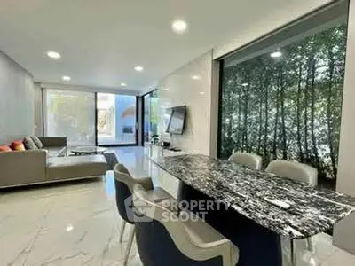 Luxurious modern living room with marble dining table and large windows offering serene garden views.