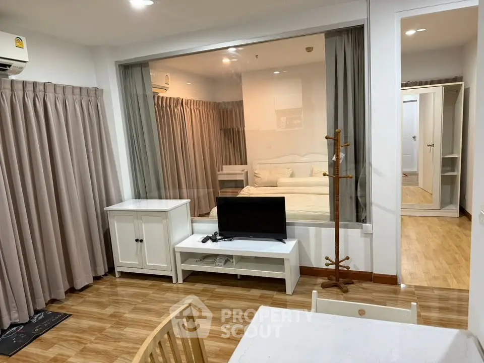 Modern studio apartment with glass partition, wooden flooring, and cozy furnishings.