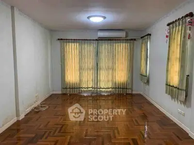 Spacious empty living room with parquet flooring and large windows.