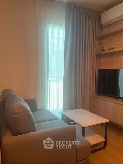 Cozy living room with modern sofa, TV, and natural light from large window.