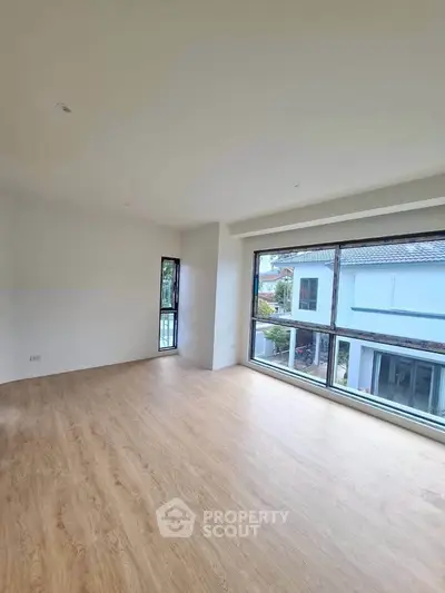 Spacious empty room with large windows and wooden flooring, offering a bright and airy atmosphere.