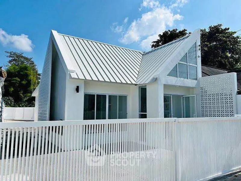 Modern white house with unique roof design and spacious outdoor area.