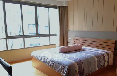 Spacious bedroom with large windows and modern decor in urban apartment.