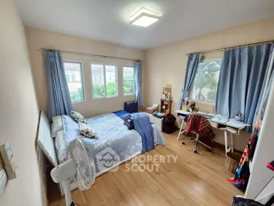 Cozy bedroom with wooden flooring, large windows, and a study desk, perfect for relaxation and productivity.