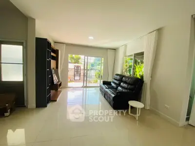 Spacious living room with modern black leather sofa and large windows opening to a balcony.