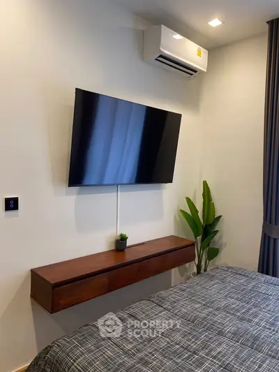 Modern bedroom with wall-mounted TV and air conditioning, featuring stylish decor and cozy bedding.