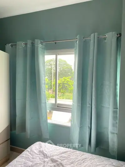 Cozy bedroom with window view and teal curtains, perfect for natural light lovers.