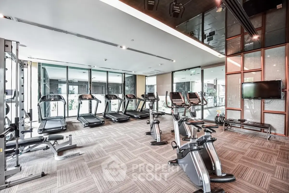 Modern gym with state-of-the-art equipment and floor-to-ceiling windows in luxury building.