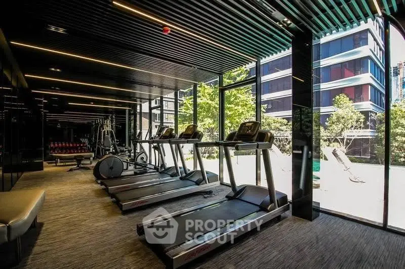 Modern gym with large windows and state-of-the-art equipment in luxury residential building.