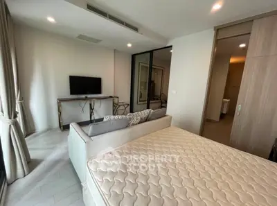 Modern bedroom with stylish decor and natural light, featuring a comfortable bed and sleek TV setup.