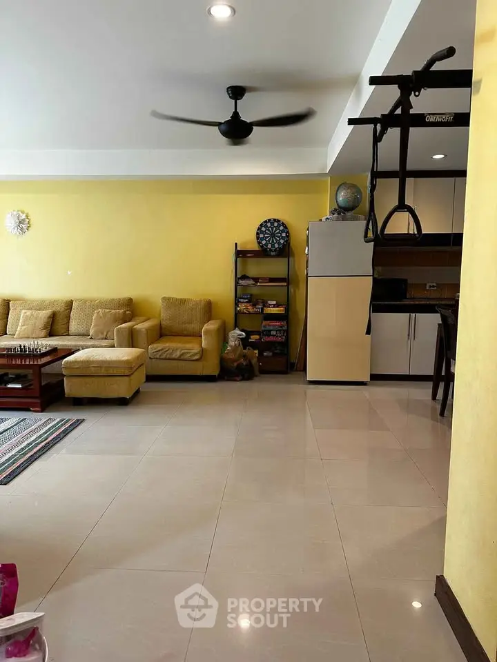 Spacious living room with yellow walls, cozy seating, and modern ceiling fan, perfect for relaxation.