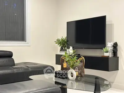 Modern living room with sleek black leather sofa and wall-mounted TV, featuring stylish decor and glass coffee table.