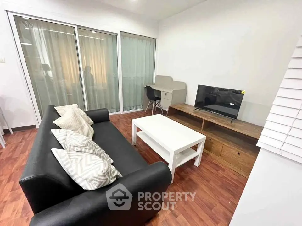 Modern living room with sleek black sofa, white coffee table, and TV setup on wooden floor.