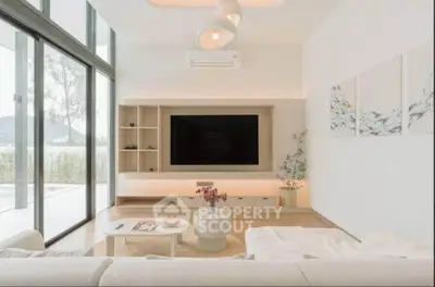 Modern living room with large TV, stylish decor, and natural light from floor-to-ceiling windows.
