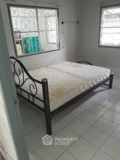 Spacious bedroom with metal bed frame and tiled flooring, ample natural light from windows.