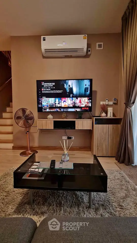 Modern living room with stylish furniture and entertainment setup, featuring a wall-mounted TV and air conditioning.