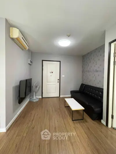 Modern living room with sleek black sofa, wall-mounted TV, and stylish decor in a cozy apartment.