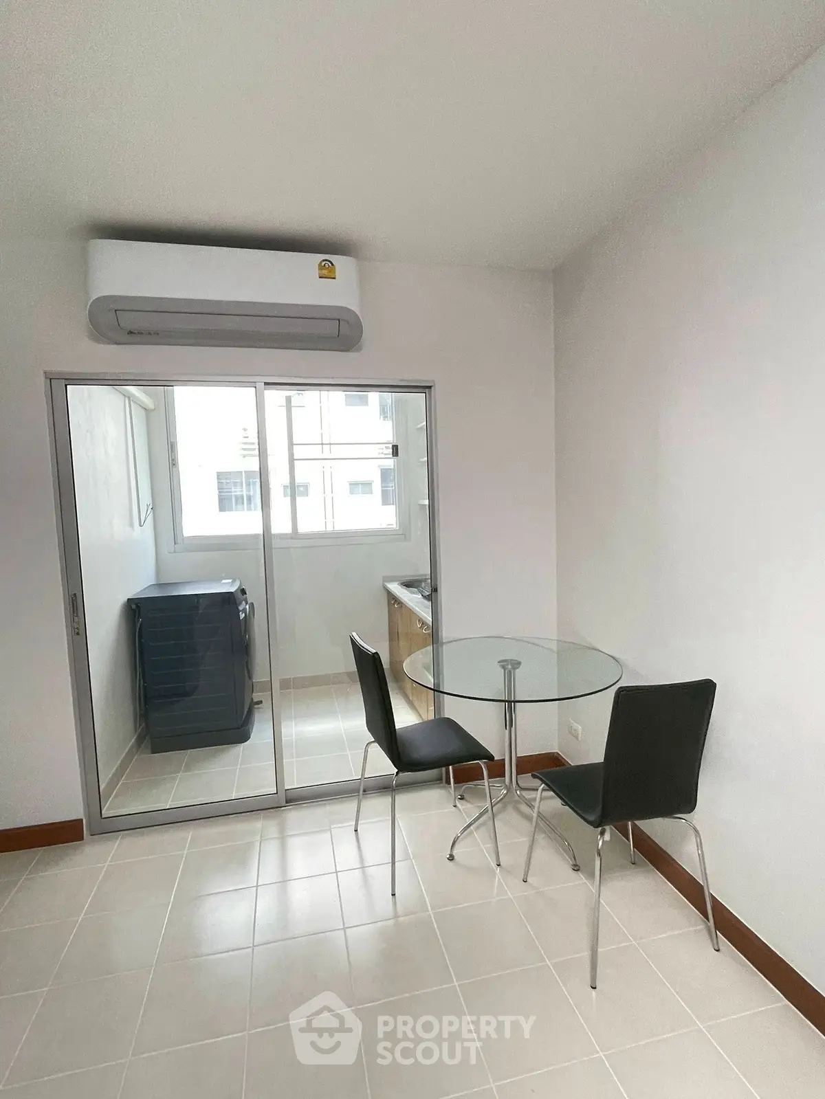 Modern dining area with glass table and chairs next to a laundry room with washing machine.