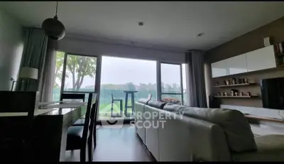 Spacious living room with large windows offering stunning green views, modern decor and cozy seating.