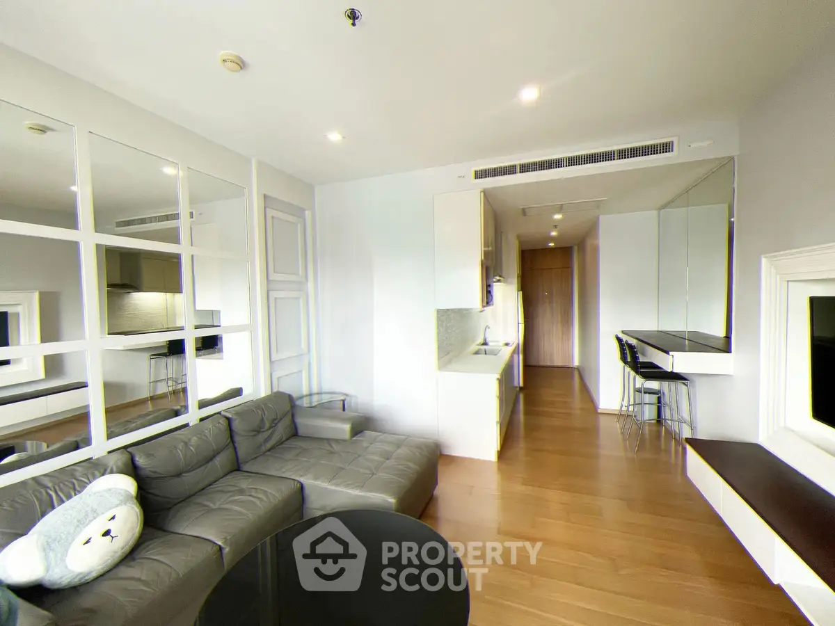 Modern living room with sleek design and open kitchen layout, featuring a cozy gray sofa and wooden flooring.
