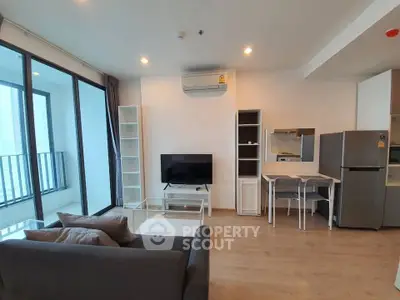 Modern living room with open kitchen, featuring sleek furniture and large windows for natural light.