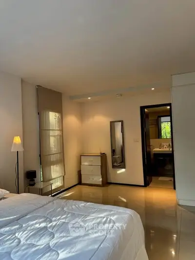 Spacious bedroom with modern decor and ensuite bathroom, featuring natural light and sleek furnishings.