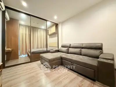 Modern living room with sleek sofa and glass partition leading to bedroom, featuring elegant wood flooring.