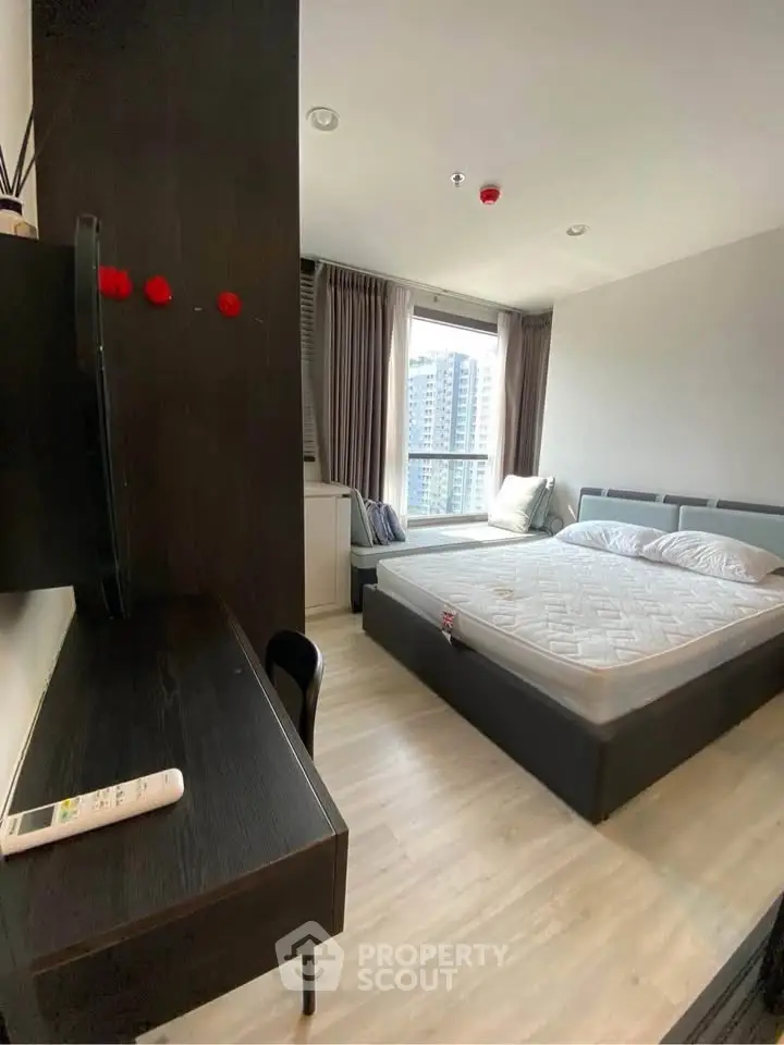 Modern bedroom with large window and city view, featuring a cozy bed and sleek workspace.