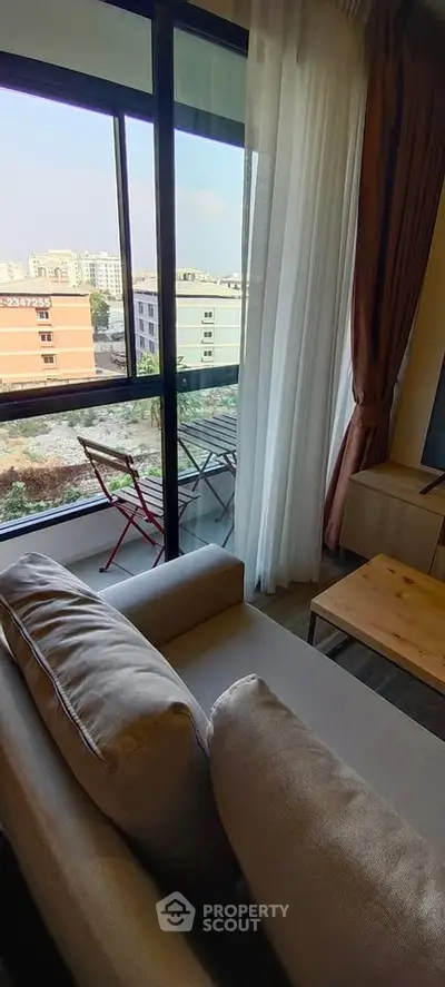 Cozy living room with large window and balcony view in modern apartment.