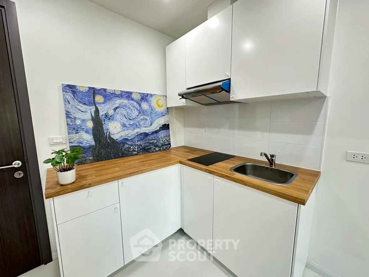 Modern kitchen with sleek white cabinets and wooden countertops, featuring a Starry Night artwork.