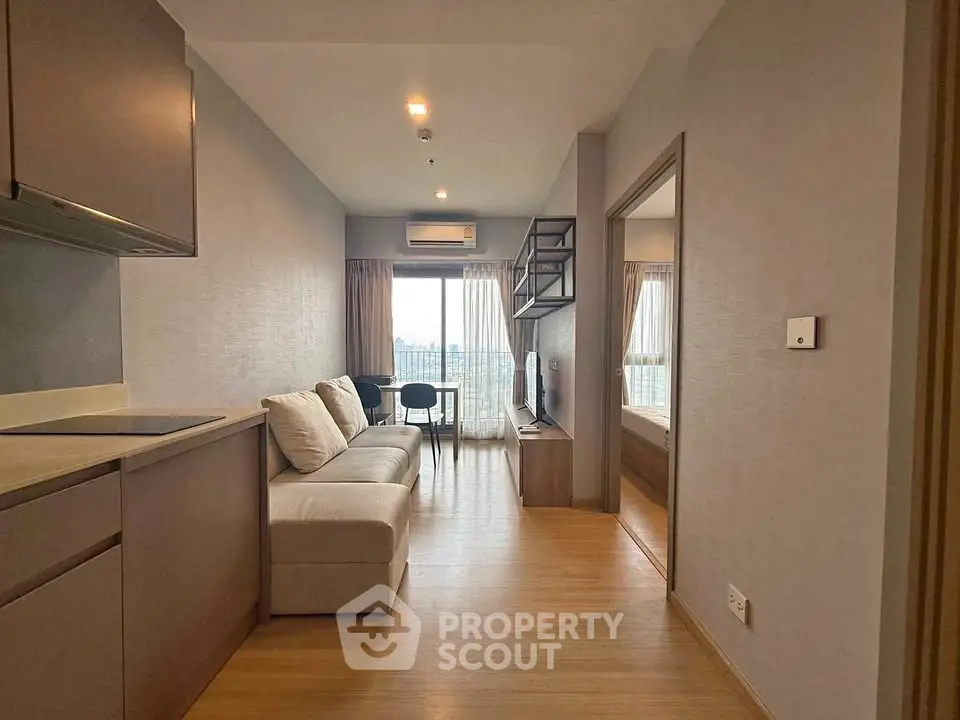 Modern living room with open layout and city view, featuring cozy sofa and sleek kitchen area.