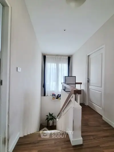 Bright hallway with wooden flooring and staircase, featuring natural light from window.